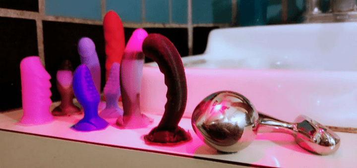 [Image: njoy Pure Plug Large stainless steel butt plug on a bathroom sink next to silicone Funkit tiny dildos]