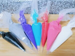 7 bags of DIY sugar cookie icing, colors mixed and ready to go: black, gray, purple, blue, red, pink, white