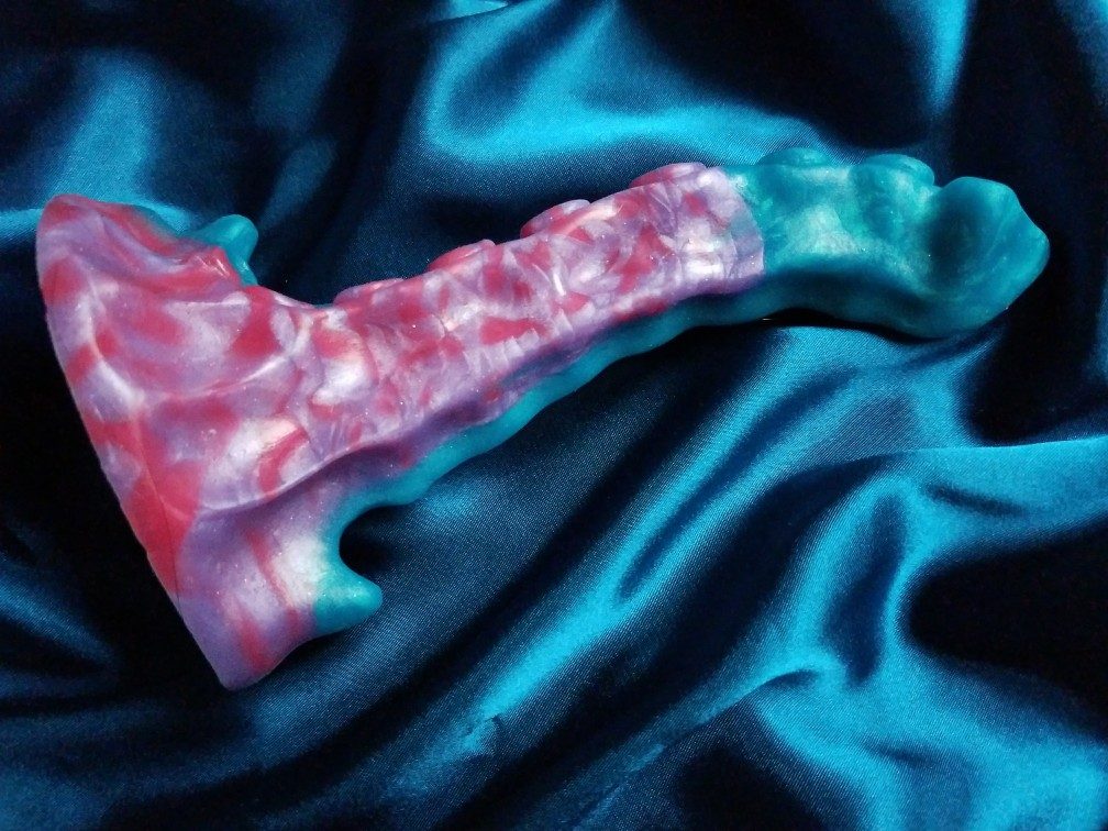 Side view of a red, purple, and teal Uberrime Xenuphora tentacle dildo