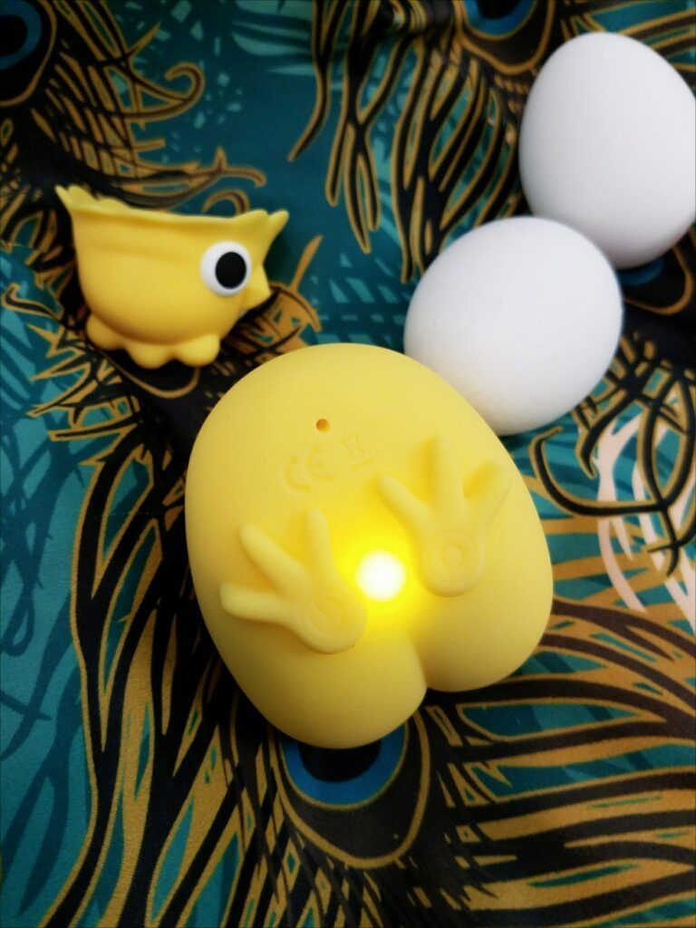 Image: a beheaded Emojibator Chickie. Its body is shown from the bottom view. Between its feet is a glowing LED indicator to let you know it's powered on