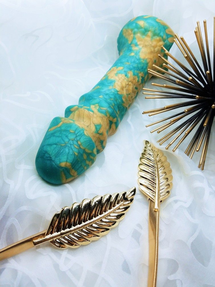 Image: a look at the Uberrime Aqua-King's silicone marbling of teal and gold. Because these dildos are handmade, no two have the exact same swirling patterns