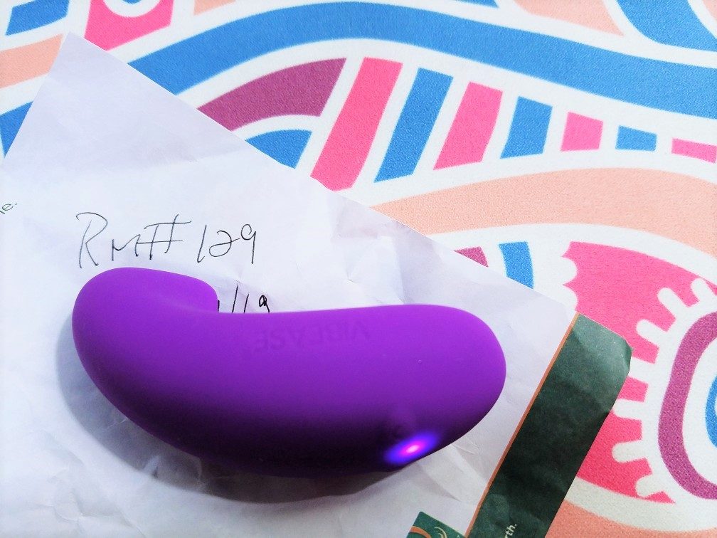 [Image: a 3/4 back/side view of a purple Vibease vibrator and its curved, hooked profile on a hotel notepad]