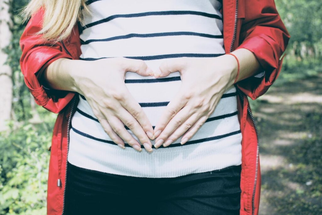 [Image: a woman whose hands form a heart shape with her thumbs and index fingers, in front of her lower abdominal area]