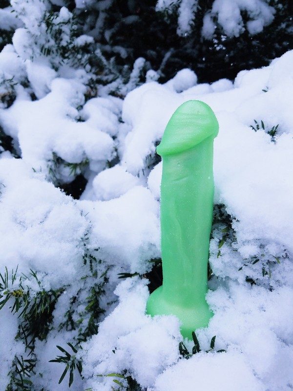 [Image: shimmery green Uberrime Supero dildo in snowy evergreen tree]