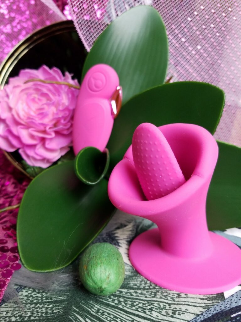 [Image: BestVibe 10-Function Rechargeable Silicone Tongue Vibrator next to faux orchid leaves]