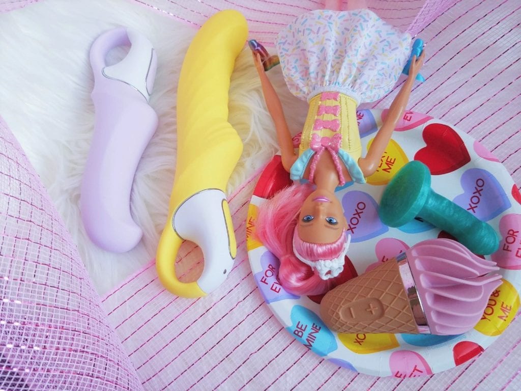 [Image: Satisfyer Charming Smile G-spot vibrator, Yummy Sunshine textured A-spot vibrator, and Sweet Treat next to doll and teenie weenies]