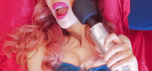 [Image: Cy Smash / the writer, a woman with red hair and pink lipstick wearing a blue bra and holding a Doxy Die Cast against her cheek]