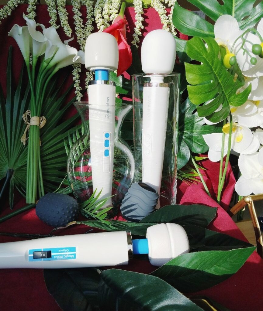 [Image: Magic Wand Plus, Magic Wand Original, Le Wand Rechargeable, and Le Wand silicone texture caps / head covers among leaves and white flowers]