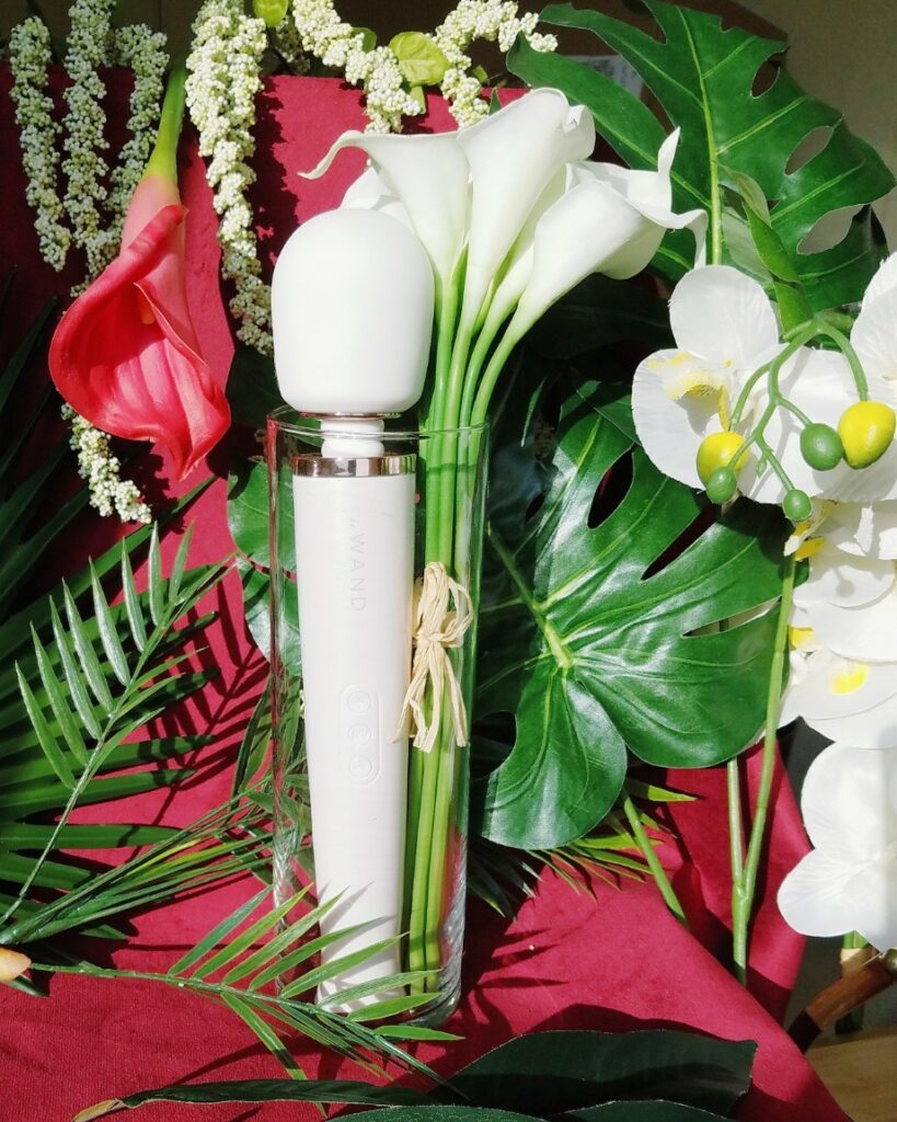 [Image: pearl white Le Wand Rechargeable body massager vibrator next to orchids and white lilies]