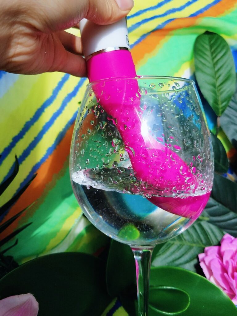 [Image: pink Xcitme Sym-B Luma rechargeable G-spot vibrator dipped in water and splashing]
