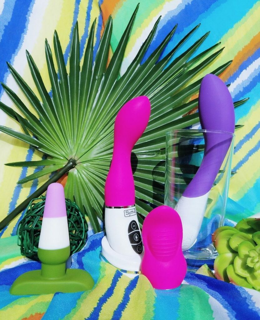 [Image: Blush Novelties genderqueer pride purple white and green striped silicone butt plug next to Xcitme Sym-B with Luma attachment, Kiki attachment, and purple LELO Mona 2]