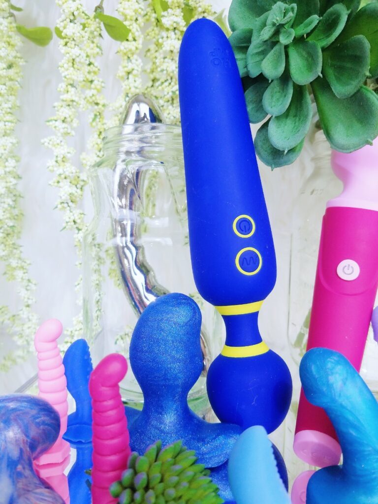[Image: a bunch of tiny silicone dildos in front of the ROMP Flip vibrator, Noje W4 wand, and Le Wand Arch stainless steel dildo]