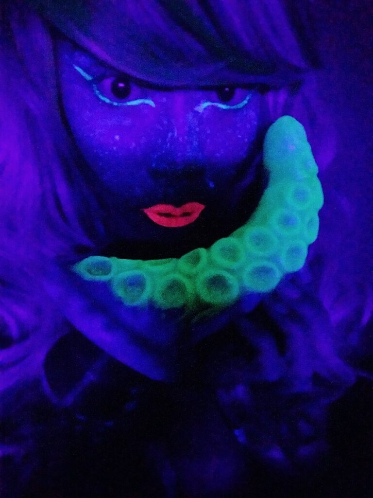 Holding Uberrime Deep Diver Glow-in-the-Dark Tentacle dildo with UV makeup in blacklight