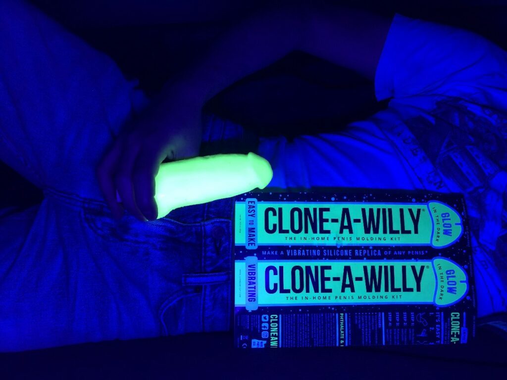 Boyfriend holding a glow-in-the-dark silicone replica of his penis. In front of him is the glowing Clone-A-Willy packaging.