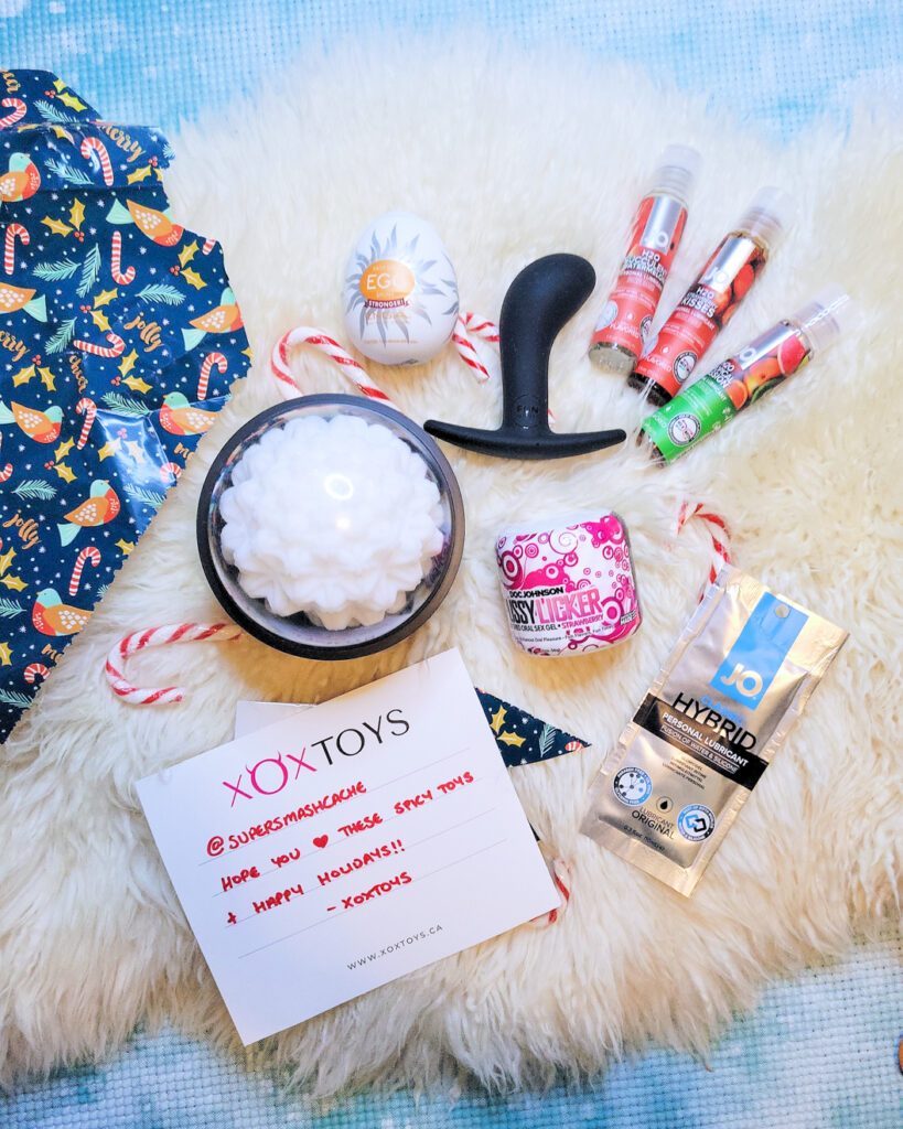 A spread featuring the Tenga Easy Beat Egg Shiny, Tenga GEO Coral sleeve, Fun Factory Bootie Medium, System JO Flavors flavored personal lubricant, Doc Johnson Pussy Licker strawberry-flavored oral sex gel, and a hand-lettered notecard from XOXtoys to Super Smash Cache