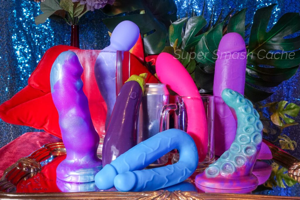 Big dildos to prepare for fisting: Pris Toys Sentinel, Dame Com wand, Self Delve eggplant/aubergine, BMS Swan Wand, NS Colours DP Pleasures double penetration dildo, Uberrime Deep Diver, and Blush Neo Elite 10" dual-density dildo next to hard cider can