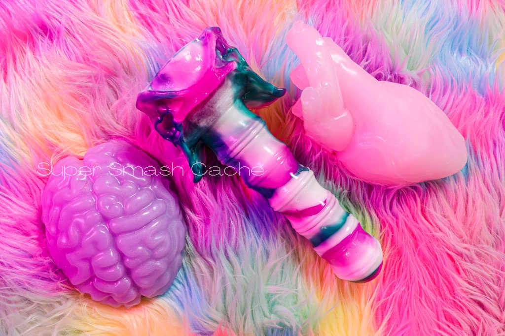 Velvet Alley Brainzzz grinder in glow-in-the-dark purple, Craven vertebral dildo, and anatomical heart silicone clitoral massager in ghost heart and glow pink