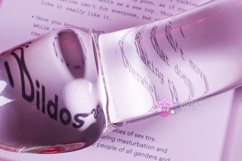 Extra large realistic mushroom tip glass dildo magnifying the word "dildos" in a book