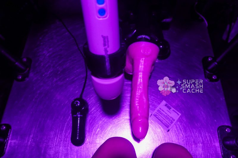Kneeling on a metal bondage table in front of the magic wand rechargeable and doc johnson power banger with dee's big daddy dante XL