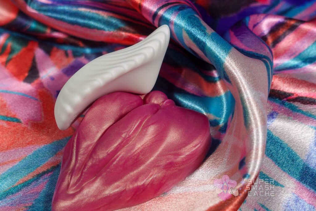 Side view of Honey Play Box Pearl 2 in white, Bluetooth app-controlled wearable vibrator on Uberrime LaBae vulva-shaped silicone grinder