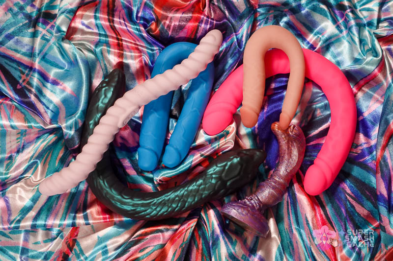 6 Silicone Double Dildos for Body-Safe DP (2026 Edition) 7 silicone double penetration dildos laid out: blush dr. skin silicone mini double dildo, tentra cor flexible unicorn horn vibrating dildo, blush ruse slim double dildo, blush temptasia twin python with adjustable core, and uberrime duobus